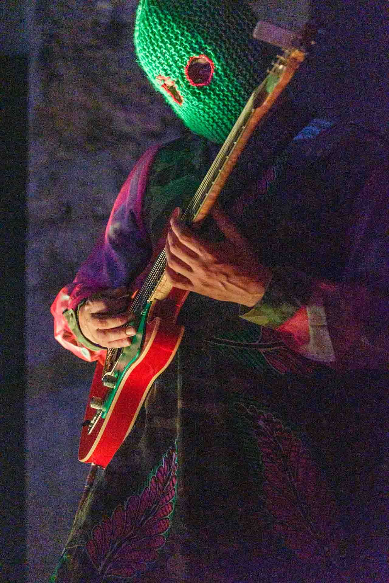 Gitarist met neon groene bivakmuts speelt op een oranje gitaar